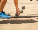 Une main saisit une boule de pétanque, prête à la lancer dans le cercle. Les règles du jeu de boules sont simples : viser le cochonnet.