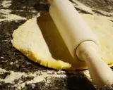 Rouleau à pâtisserie aplatissant une pâte à foncer sur un plan de travail fariné.