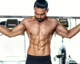 Ein Mann mit stark definierten Bauchmuskeln hält eine Langhantel im **cutten gym**.