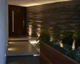 Ingresso con gradino interno illuminato, porta scura, muro in pietra e piante.