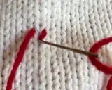 Nål med rött garn syr ihop stickat med maskstygn.