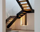 Scala interna con gradini in legno e struttura metallica nera. Il parapetto in vetro trasparente dona leggerezza al design moderno.