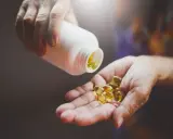 Une main verse des gélules dorées, la vitamine du soleil, dans une autre main.