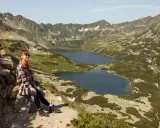 Kobieta odpoczywa na szlaku w Dolinie Pięciu Stawów. W tle rozciągają się góry i jeziora.