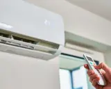 Mano ajustando el aire acondicionado a la temperatura ideal para ahorrar energía. La unidad muestra 21 grados.