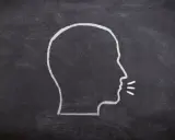 Kredą narysowany profil głowy z liniami symbolizującymi dźwięk wydobywający się z ust, ukazujący fałdy głosowe podczas mówienia.