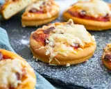 Mehrere mini pizza mit geschmolzenem Käse und Tomatensauce auf einem dunklen Untergrund, bestreut mit etwas Mehl.