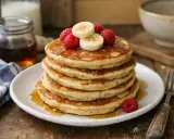 Pile de pancakes sans oeuf, garnis de framboises et rondelles de banane, arrosés de sirop d'érable. Un délice pour le petit-déjeuner.