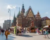 Wrocław stare miasto tętni życiem. Ludzie spacerują po Rynku, podziwiając zabytkowy ratusz i kolorowe kramy.