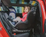 Mała dziewczynka w czerwonej kurtce siedzi w foteliku samochodowym Britax Römer.