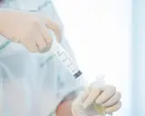 Ręce w rękawiczkach przygotowują pobranie płynu mózgowo rdzeniowego do analizy.