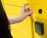 Dłoń zbliża telefon do żółtego Paczkomatu InPost, aby zapłacić.