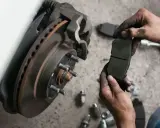 Mechanik trzyma zużyte klocki hamulcowe. Sprawdź wymiana klocków hamulcowych cena i zadbaj o bezpieczeństwo.