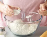 Kobieta dodaje do mąki w szklanej misce biały proszek, kluczowy składnik proszku do pieczenia.