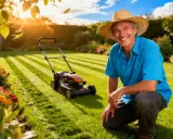 Un homme souriant, chapeau de paille, prêt à tondre la pelouse. Le soleil brille sur le jardin, les fleurs sont éclatantes. C'est le moment idéal pour savoir quand tondre la pelouse.