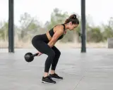 Frau in Sportkleidung macht einen Kettlebell Swing im Freien.