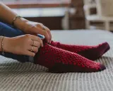 Manos ajustando calcetines rojos y morados tejidos a mano con agujas circulares.