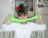 Bambina sorridente con slime verde brillante, un divertente esperimento per la ricetta slime fatta in casa.