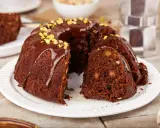 Pyszna babka na oleju, polana czekoladą i posypana pistacjami, z kawałkiem na talerzyku.