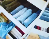 Cajones de armario organizados tras una **limpieza de armario**. Ropa doblada y ordenada por color y tipo, predominan los vaqueros y prendas en tonos tierra y azules.