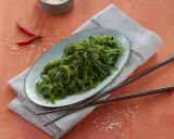 Ein Teller mit leckerem Wakame Salat, garniert mit Chilis und Sesam. Dazu liegen Holzstäbchen bereit.