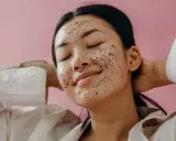 Une jeune femme au visage couvert d'un masque exfoliant scintillant, profitant d'un moment de détente. Elle nous rappelle pourquoi exfolier sa peau est essentiel pour un teint éclatant.