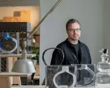 Matti Klenell, en man med glasögon, står bland sina konstverk av glas.