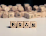 Drewniane kostki z literami tworzą napis "EXAM". Zastanawiasz się, na jakim poziomie jest matura podstawowa z angielskiego?