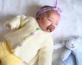 Un bebé con un suéter tejido a dos agujas y un conejito de peluche. El suéter es un muestrario de puntos a dos agujas para bebes.