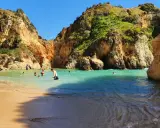 Sonnige Bucht mit Felsen und türkisfarbenem Wasser. Menschen baden und genießen das milde Wetter im **Portugal im Dezember**.
