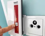 Fritz! WLAN Repeater verbessert das Signal, um **WLAN durch Betondecke** zu leiten. Ein Finger drückt auf die WPS-Taste.