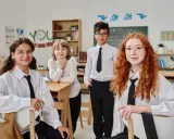 Vier Schüler in weißem Hemd und schwarzer Krawatte im Klassenzimmer. Ein Vergleich des Schulsystems Finnland und Deutschland könnte hier beginnen.