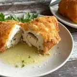 Złocisty kotlet de volaille, przekrojony na pół, odsłaniający soczyste wnętrze z ziołami, pływa w maśle.