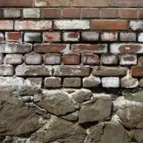 Alte Ziegelwand mit deutlichen Spuren von Salpeter. Die unteren Steine sind grob behauen und bilden eine solide Basis.