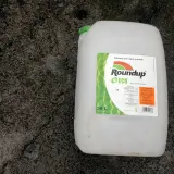En stor vit dunk med etikett för Roundup ECO, ett glyfosatbaserat ogräsmedel, står på en grå, fuktig yta.