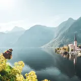 Schmetterling auf blühendem Zweig vor malerischem Dorf am See, umgeben von majestätischem Gebirge Europas.