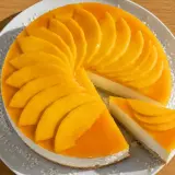 En krämig mango cheesecake med färska mangoskivor som pryder toppen. En bit är uppskuren och visar den läckra fyllningen.