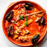 Un invitante brodetto di pesce in terracotta, ricco di cozze, vongole e gamberi, con un tocco di basilico fresco.