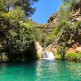Un puente colgante cruza un **río verde** en Granada, con una cascada y vegetación exuberante.
