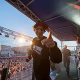 Kosi z JWP Crew w wieku około 30 lat, na scenie z mikrofonem, wskazuje palcem na widownię.