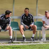 Trzech mężczyzn siedzi na ławce. Dwóch w strojach sportowych, jeden w białej koszulce. To trener Lechii Gdańsk i jego współpracownicy.