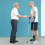 Arzt schüttelt Hand eines Patienten mit Krücken und Orthese am Fuß nach einer Calcaneusfraktur.