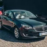 Elegancki, ciemnozielony Buick Regal z chromowanymi felgami stoi na brukowanej ulicy.