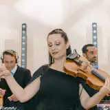 Une violoniste joue lors d'un mariage, avec des DJs en arrière-plan. Un prix DJ mariage pour une ambiance unique.