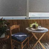 Przytulna loggia w bloku z drewnianym krzesłem, stolikiem i roślinami. Idealne miejsce na poranną kawę.