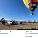 Balon na gorącym powietrzu wznosi się na błękitnym niebie. Na ziemi stoją ludzie, samochody i amerykańska flaga. Obraz porównuje formaty HEIC i JPG.