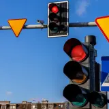 Sygnalizacja świetlna z czerwonym światłem, znaki drogowe: ustąp pierwszeństwa, przejście dla pieszych i rowerzystów.