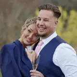 Ett lyckligt par, som från Love is Blind, firar med champagne. Rasmus ler stort, hans partner lutar sig mot honom.