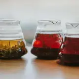 Trzy szklane dzbanki z zaparzonymi herbatami: jasnożółtą z liśćmi, czerwoną i ciemnoczerwoną, być może lapsang souchong.