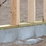 Solidny fundament pod dom szkieletowy, z drewnianymi słupkami i betonową podwaliną, gotowy na kolejne etapy budowy.